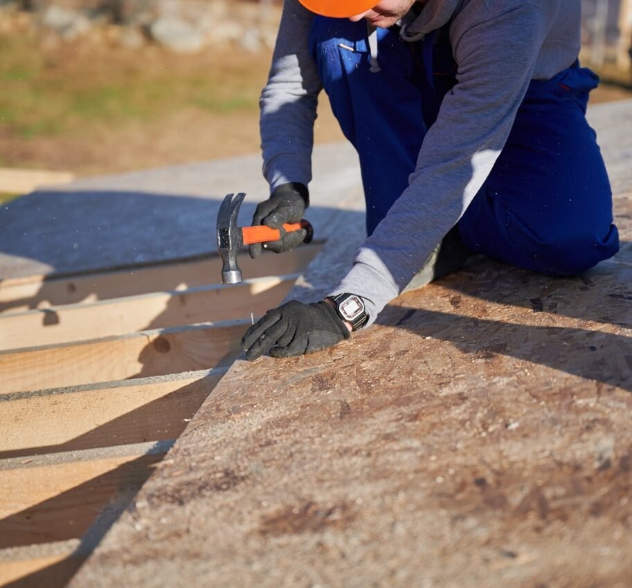 Carpenter hammering nail into OSB panel while building wooden frame house.